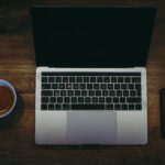 macbook pro beside white ceramic mug on brown wooden table