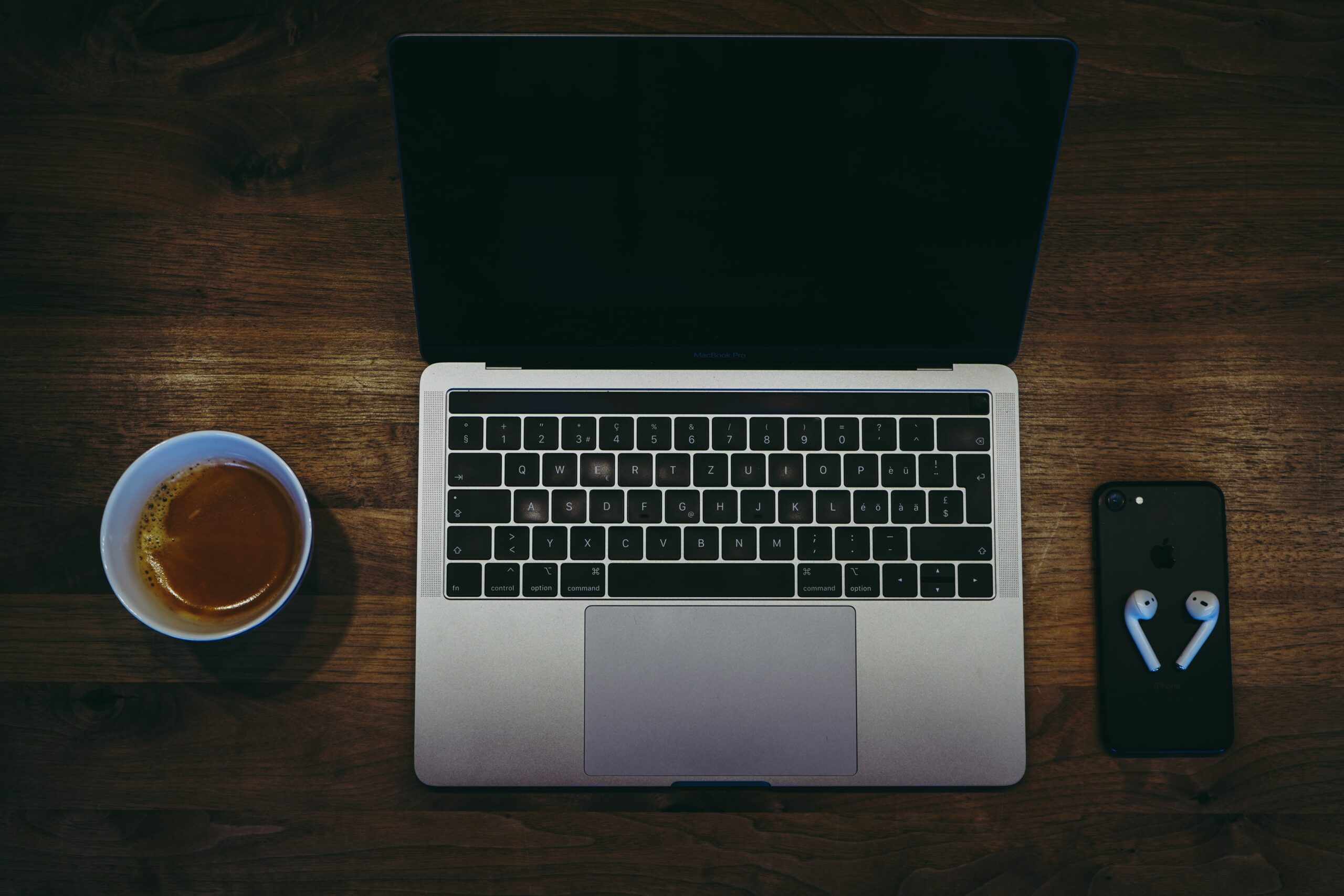 macbook pro beside white ceramic mug on brown wooden table